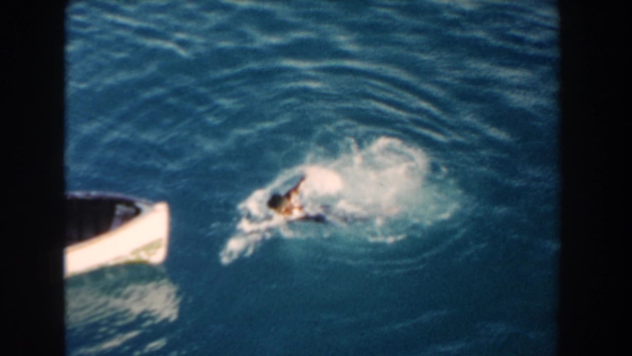 Swimmer near the side of a small white boat in rippling blue water.
