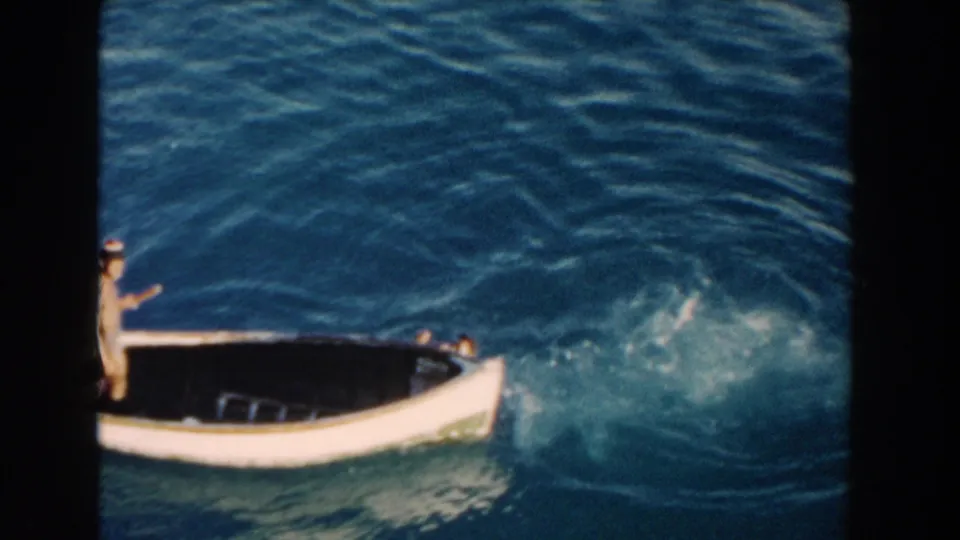 1960 Miami home-movie frame showing part of a white open boat and a swimmer in the water beside it.