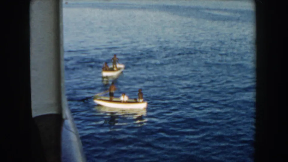 Wider 1960 Miami frame with two small white boats on blue water, seen from beside a larger vessel or dock edge.