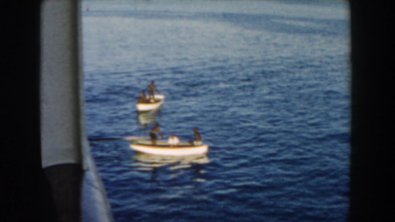 1960 Miami home-movie frame showing two small rowboats with people on calm blue water, viewed from inside or beside a larger vessel.