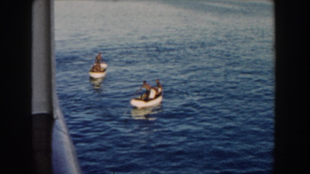 Two small boats with people on calm blue water, seen from beside a vessel.