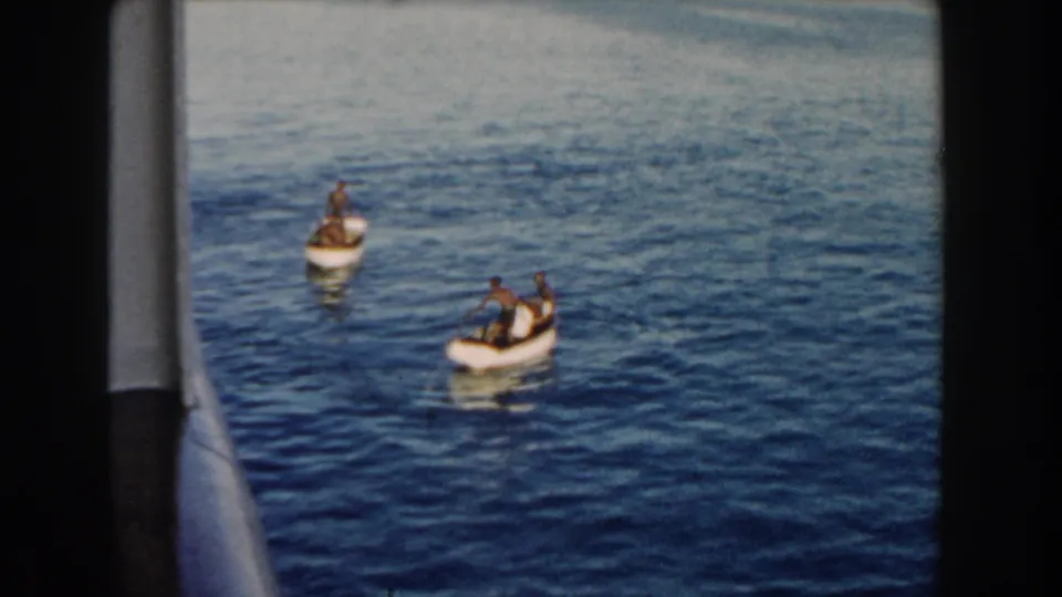 1960 Miami harbor view of two small boats carrying people on calm water, filmed from a nearby moving vessel.