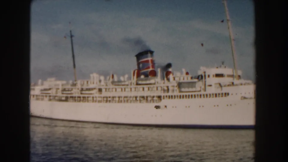 1960 Miami-area 8mm frame showing a white ocean liner with a red-and-black funnel moving across calm water.