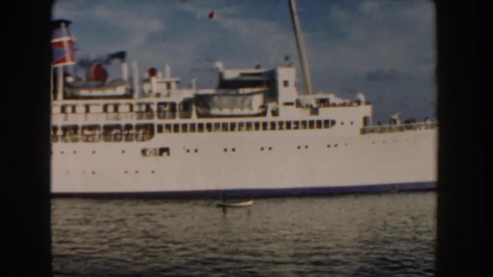 1960 Miami 8mm frame showing a distant white passenger ship across the water with a red and blue funnel and a small boat in front.