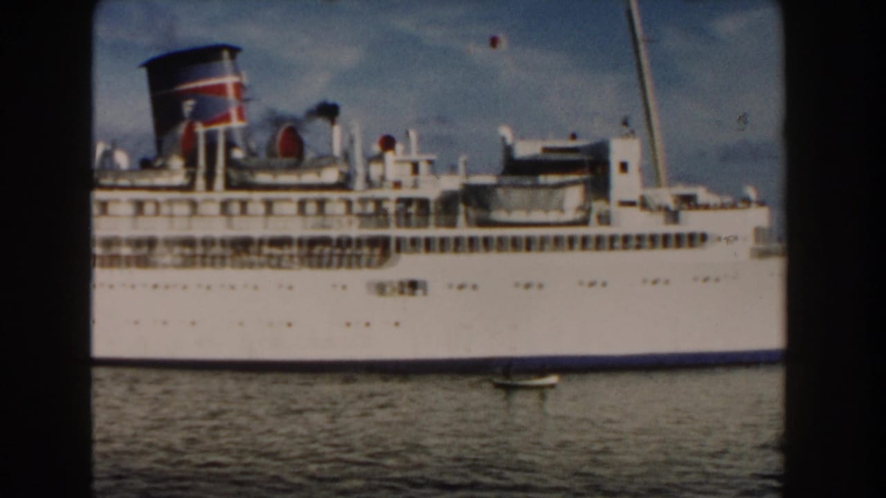 White multi-deck ship fills the frame above rippled water, with a small boat below.