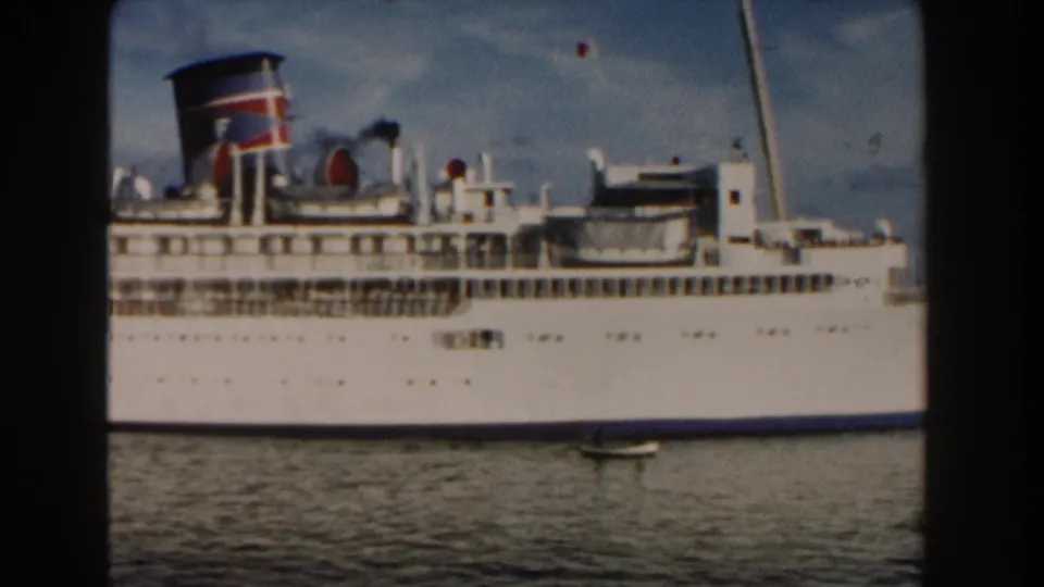 1960 Miami home-movie frame of a large white multi-deck ship with a colored funnel seen from across rippled water.