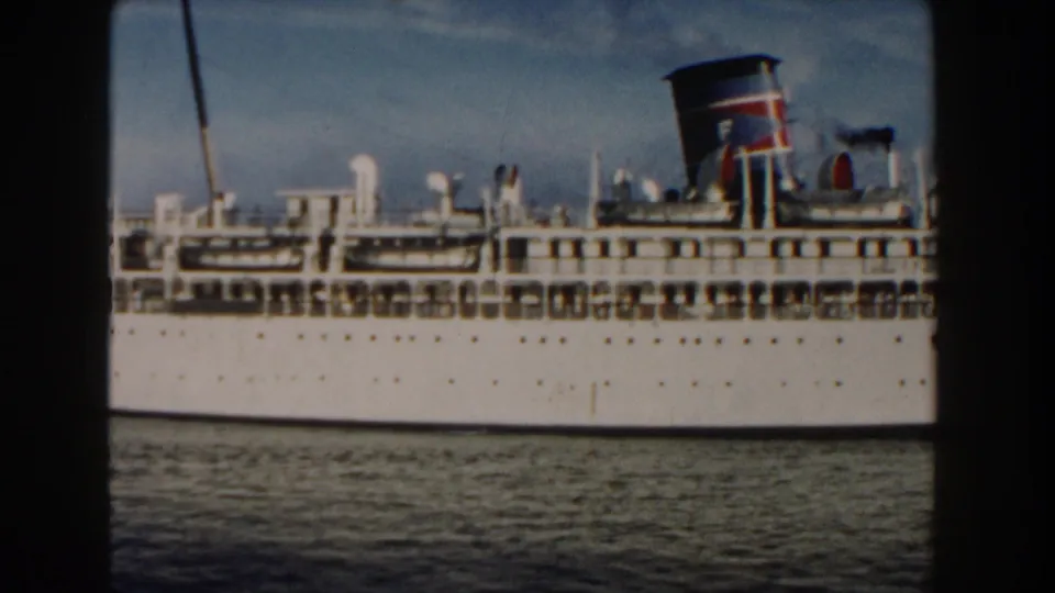 1960 Miami home-movie frame showing the side of a white passenger ship with rigging, stacked decks, colored funnel, and foreground water.