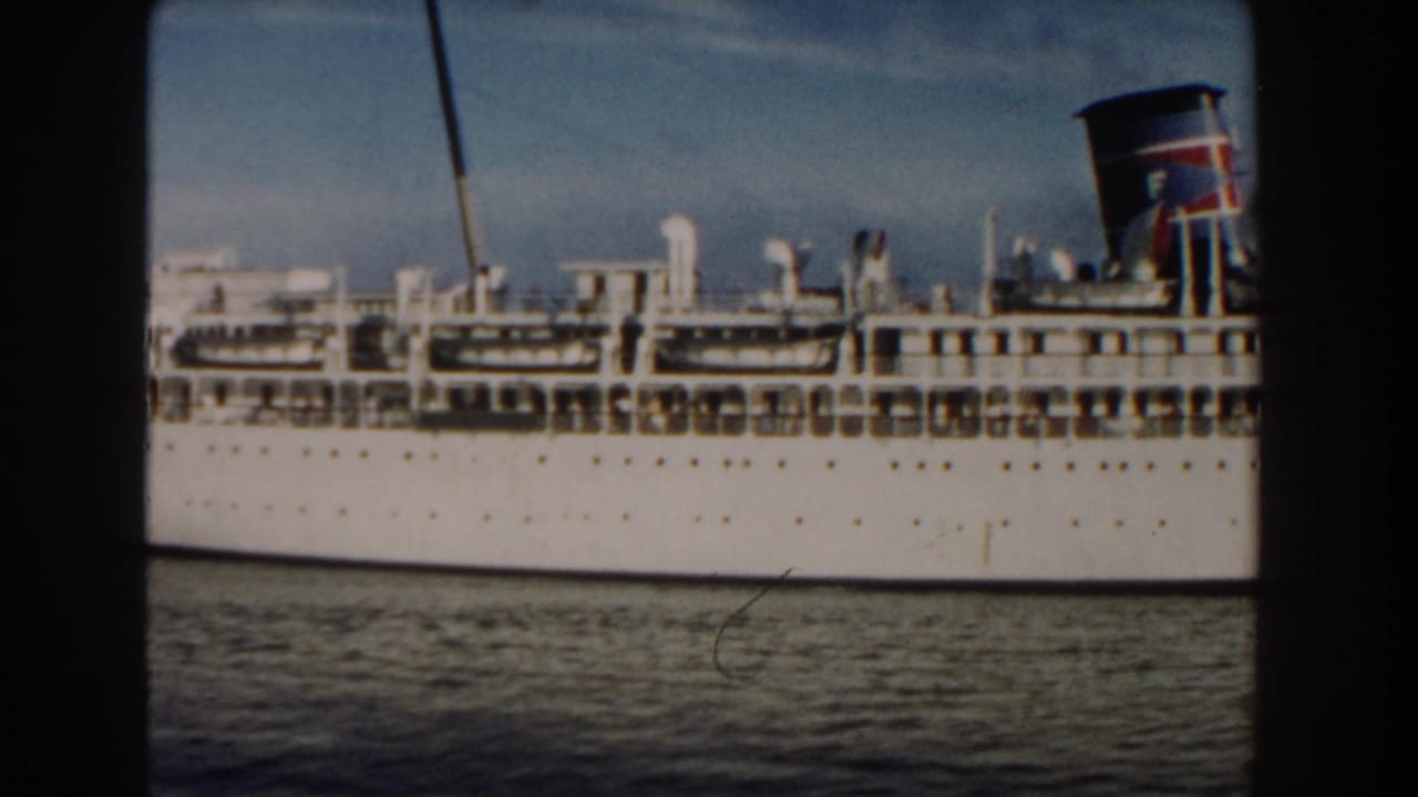 1960 Miami-area 8mm frame of a white cruise ship moving across calm blue water, with deck railings, funnel markings, and film gate edges visible.