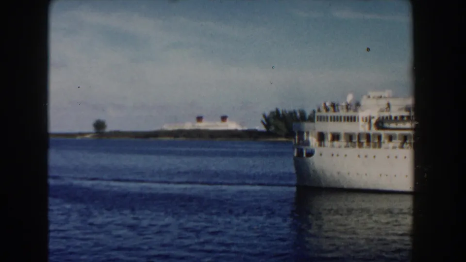 1960 Miami-area 8mm frame with the cruise ship exiting at right, leaving blue water, pale sky, shoreline forms, and a distant vessel in view.