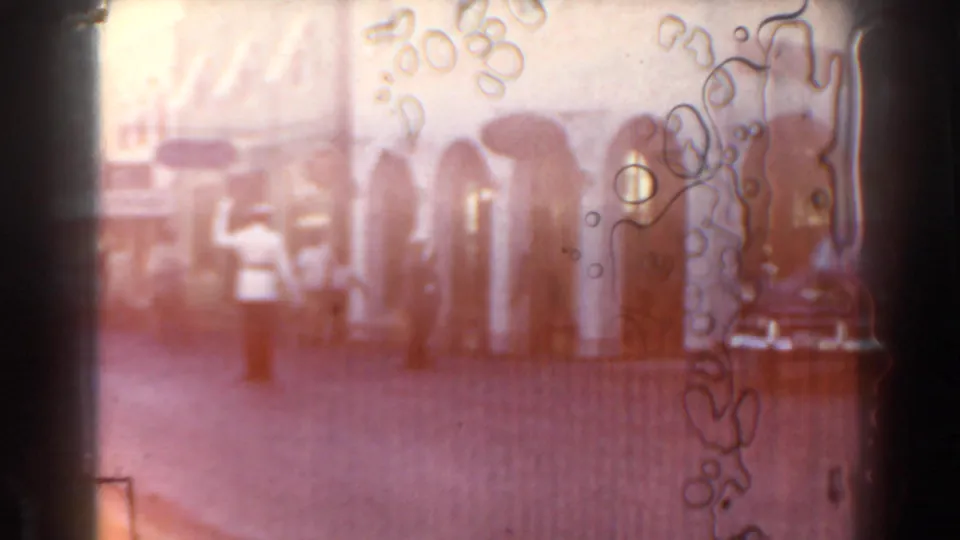 Overexposed 8mm frame from the Miami street clip, with pedestrians faintly visible through warm flare and edge markings.