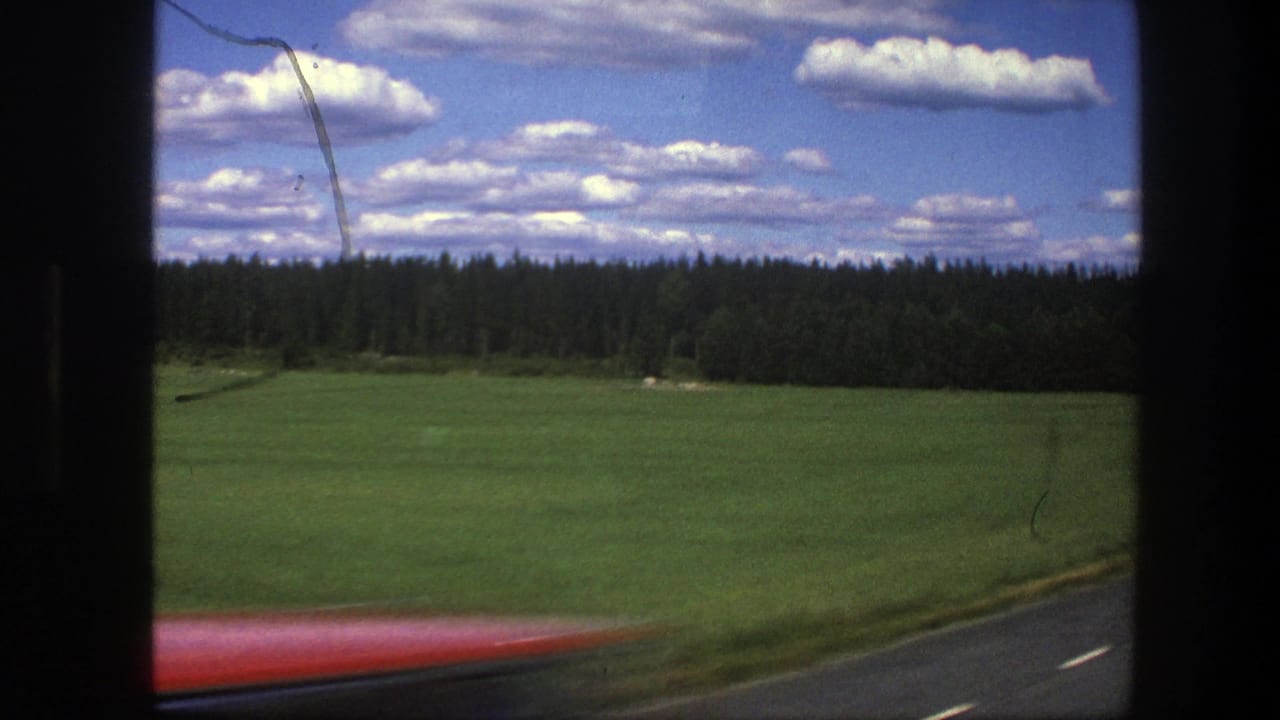 Roadside field and forest with a blurred red car passing along the lower edge.