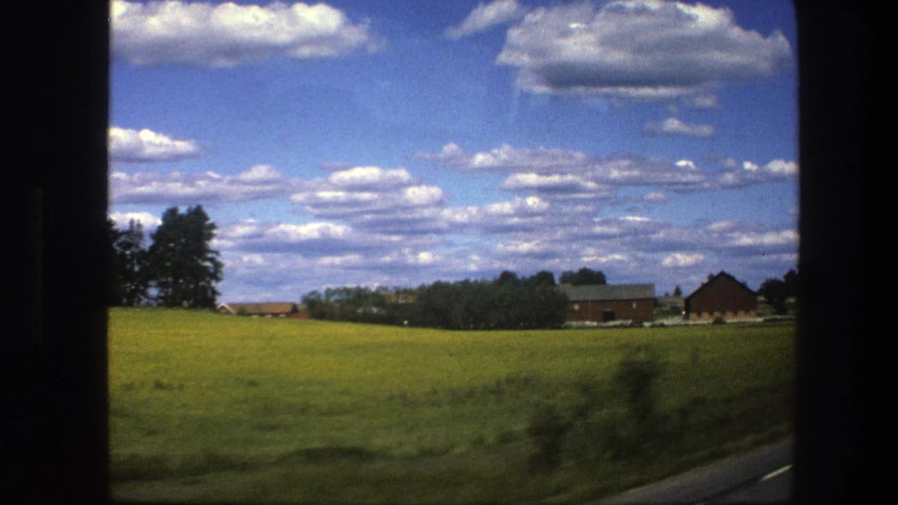 Open farmland with red buildings and trees beneath a clouded sky.