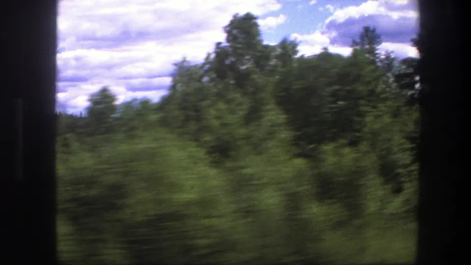 1975 Swedish travel footage frame with fast-moving green roadside trees, soft focus, and a bright partly cloudy sky.