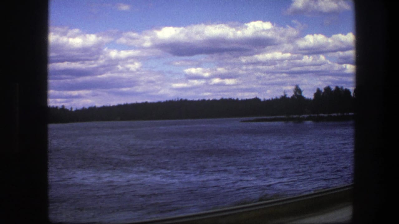 Lake seen through dark vehicle window edges with distant trees and clouds.
