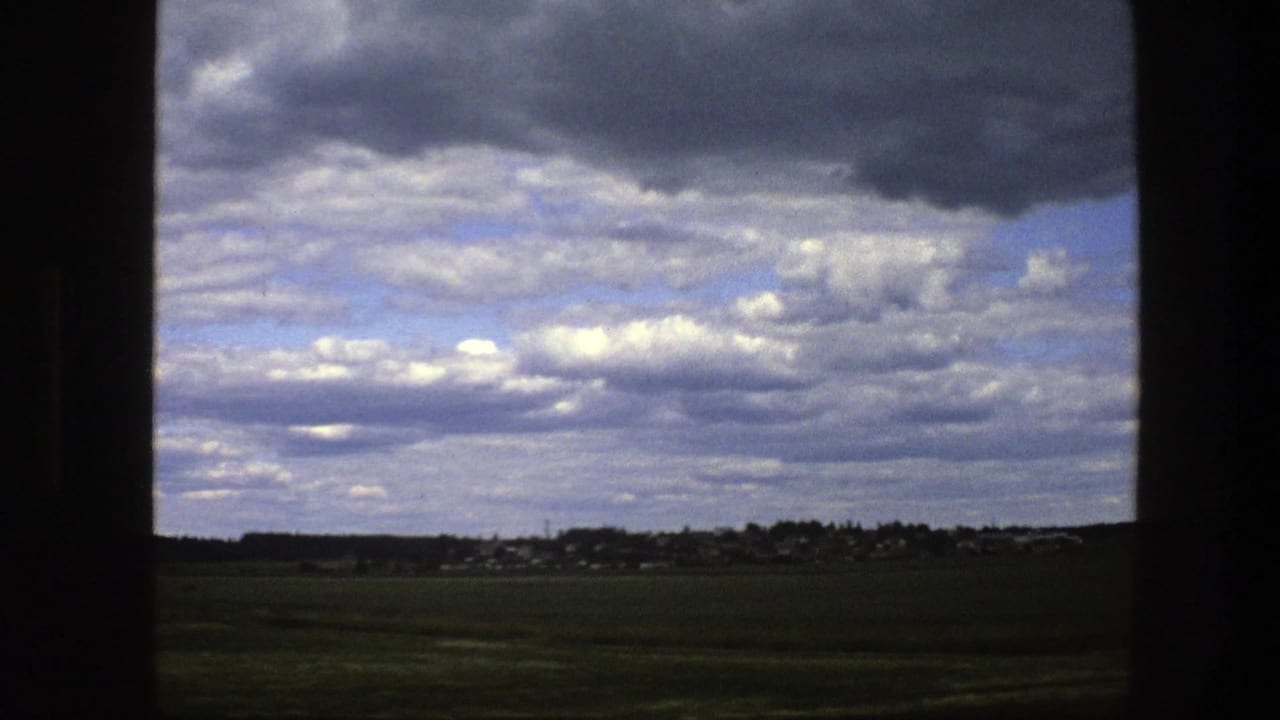 Broad cloudy sky over green fields and a distant low horizon, bordered by dark window trim.