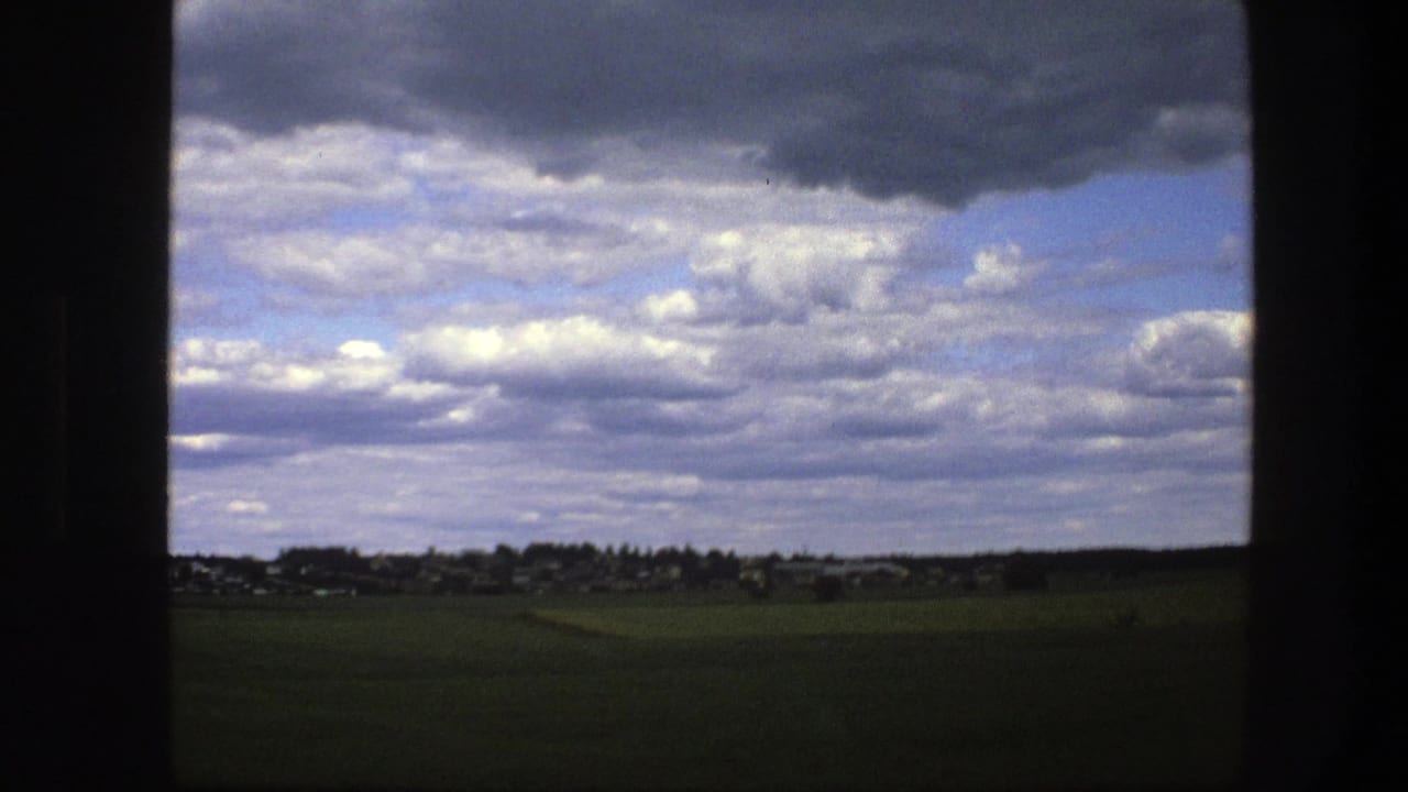 Green fields and distant village beneath heavy clouds.