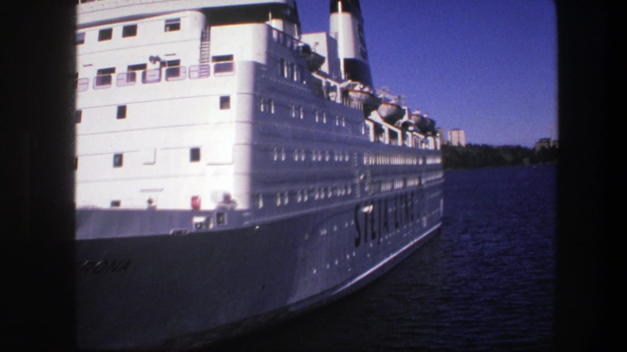 White cruise ship hull and upper decks seen close beside dark blue river water.