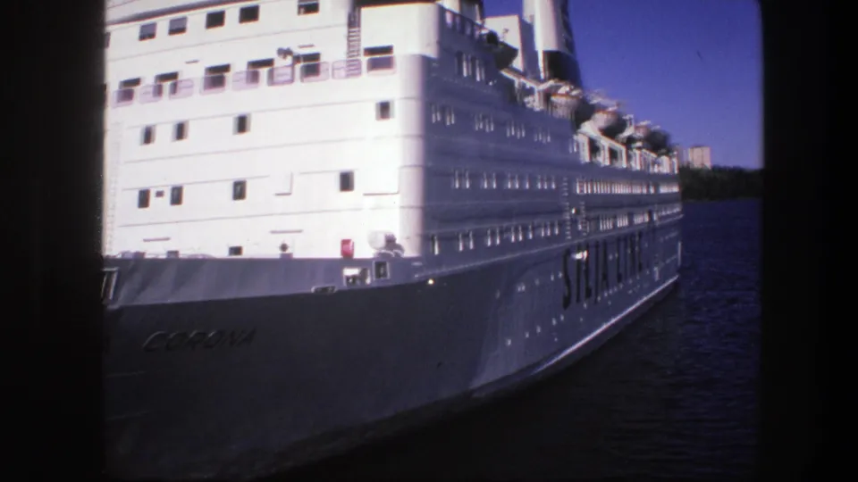 1975 Sweden 8mm frame with the passenger ship closer in view, showing its white hull, windows, lifeboats, and partial vessel name.