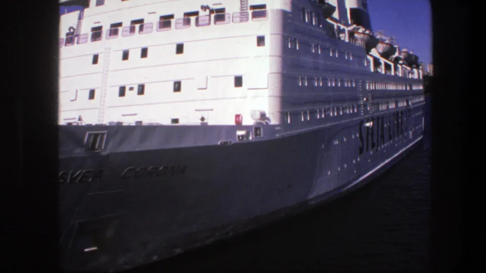 1975 Sweden 8mm frame showing the large white passenger ship close to camera, with visible hull lettering, deck windows, and river water.