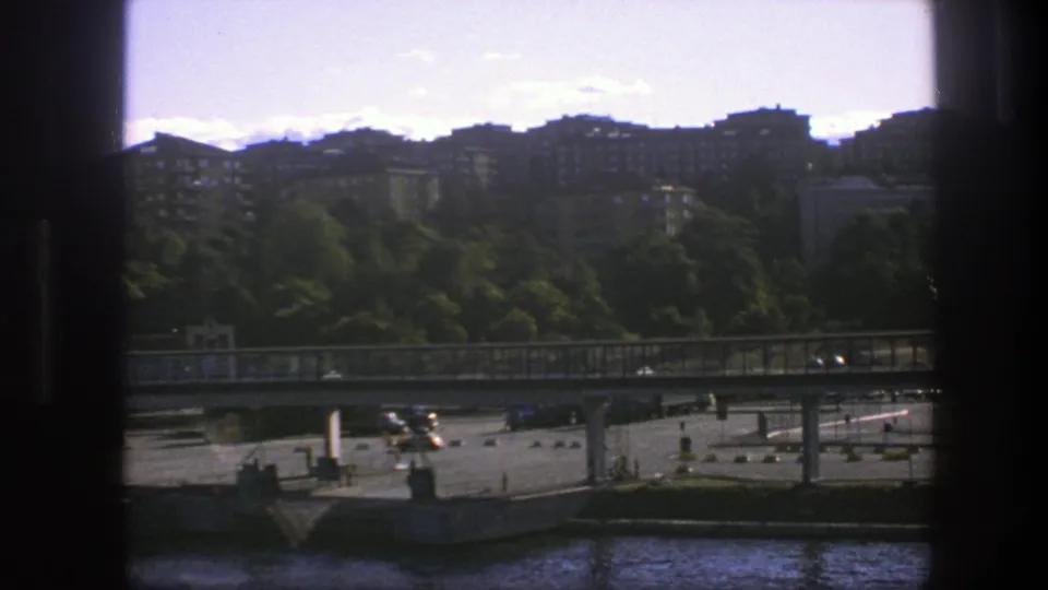 1975 Sweden waterfront frame showing the bridge and lower traffic area below trees and residential apartment blocks.