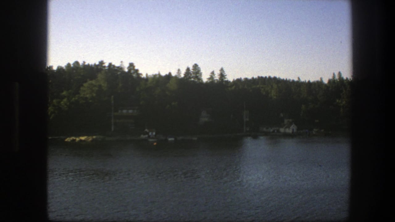 Lake seen through dark window edges with forested shoreline and small distant buildings.