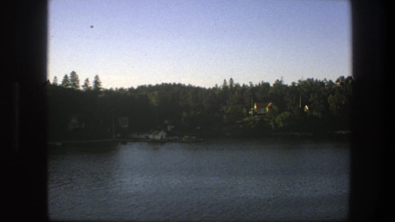 Dark boat-window framing over rippled water and a wooded Swedish shoreline.