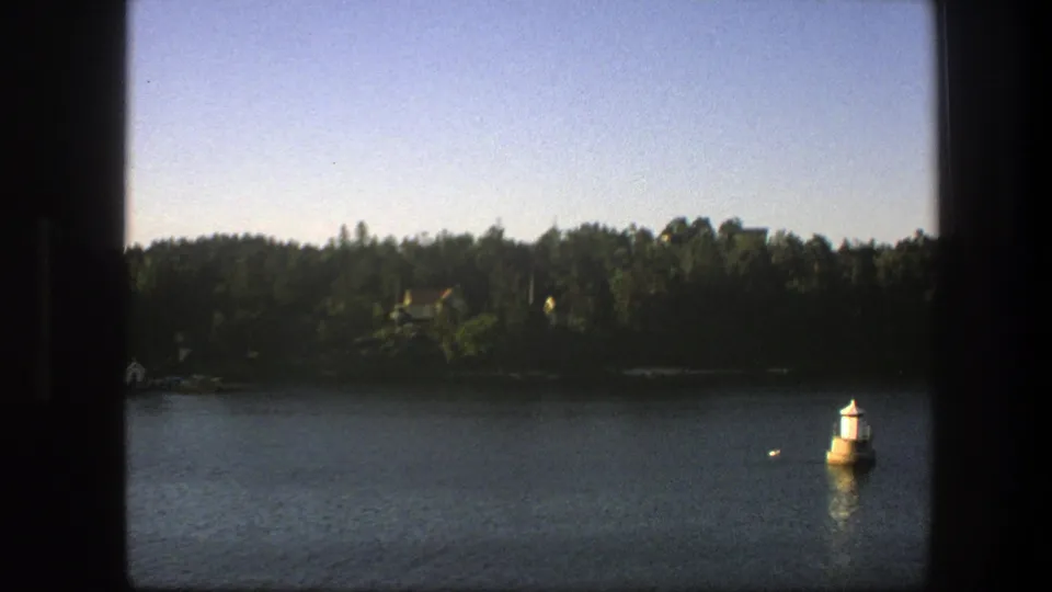 Final 1975 Sweden frame shows rippled water, a wooded shore with small houses, and a buoy at lower right, reinforcing the boat-based viewpoint.