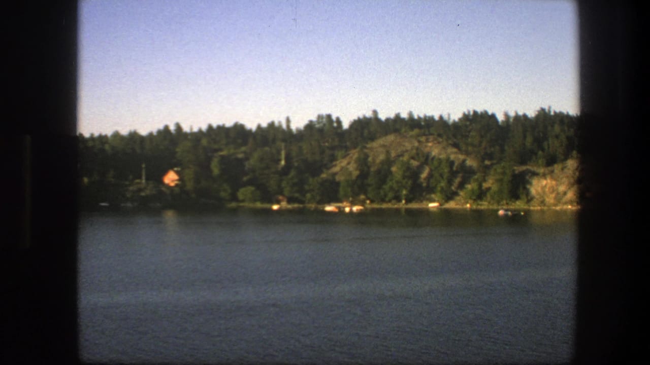 Calm lake seen past dark window edges with forested rocky shoreline and blue sky.