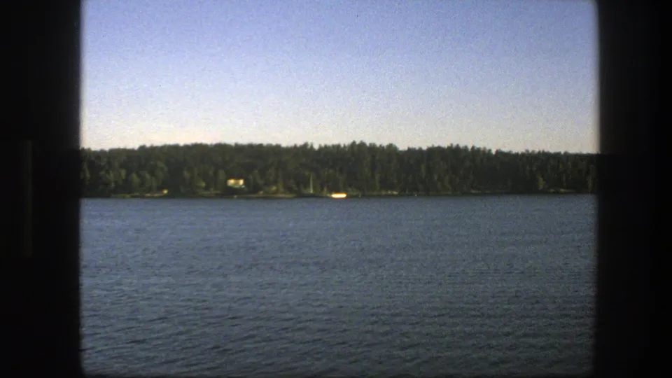 1975 Swedish 8mm frame of rippled lake water and a forested far shore with small pale shoreline details.
