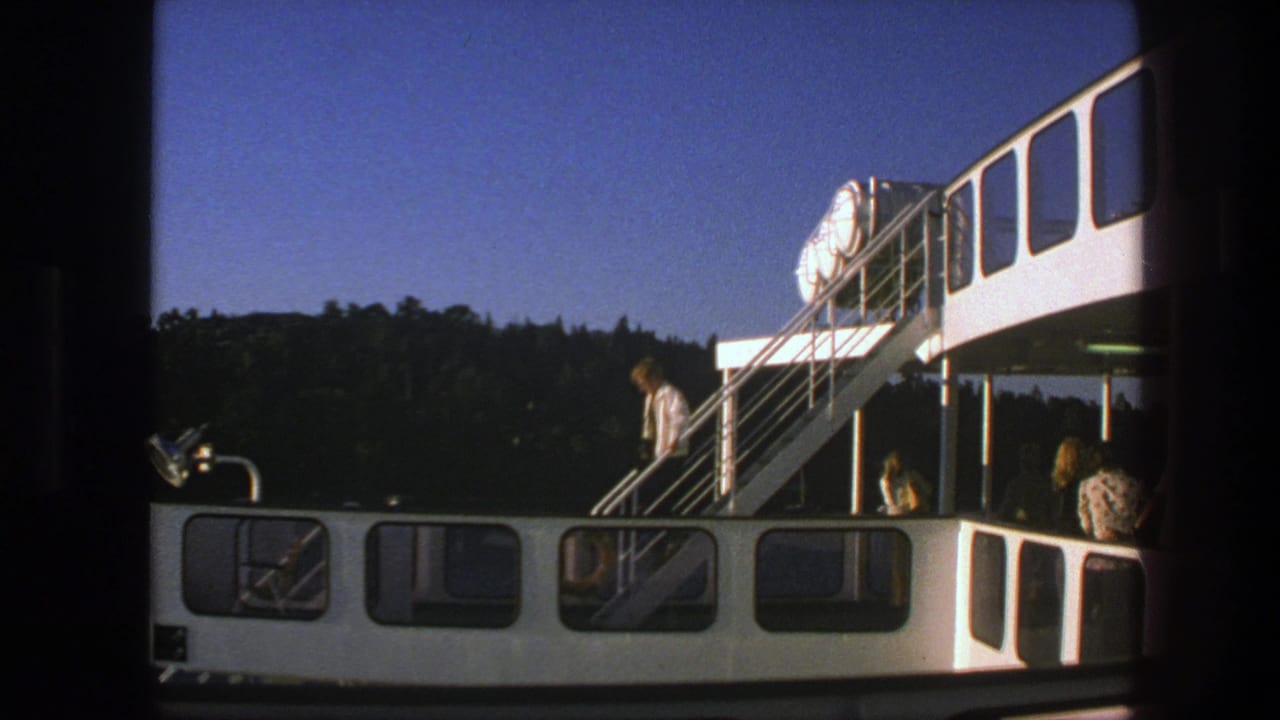 Man in a white jacket walks down ferry stairs above passengers on the lower deck.