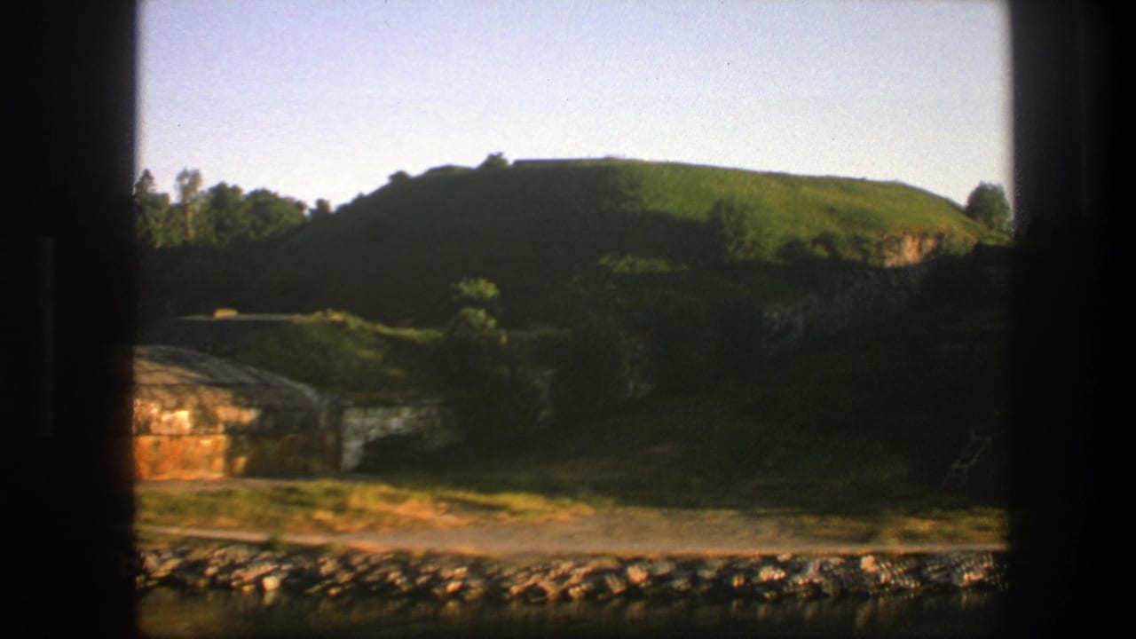 Window-framed view of a green hillside above a rocky riverbank.