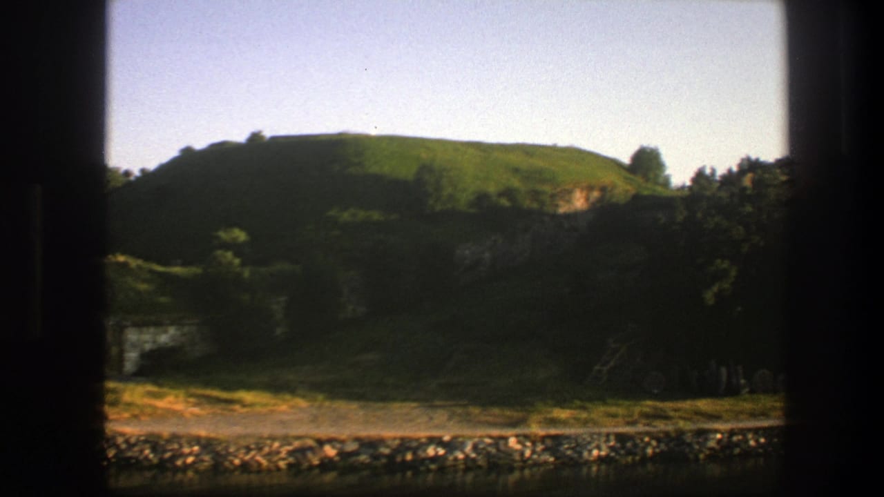 Green hill and shaded riverbank seen through a window frame.