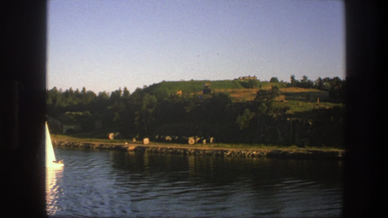 Small sailboat on calm water near a wooded shore and hillside.