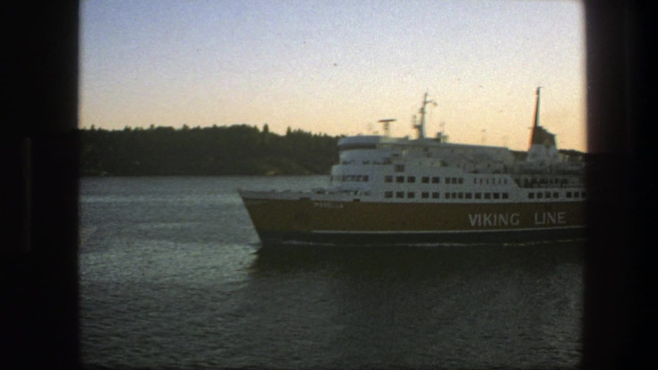 Viking Line ferry partly visible on calm water near a wooded shore.