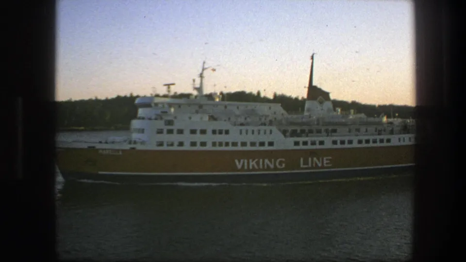 1975 Sweden 8mm frame showing a Viking Line passenger ferry moving across calm water near a wooded shoreline at sunset.