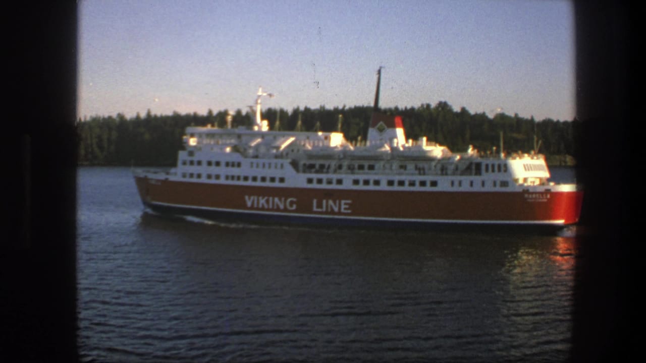 1975 Sweden 8mm frame of a red-and-white Viking Line ferry moving across calm water near a tree-lined shore.