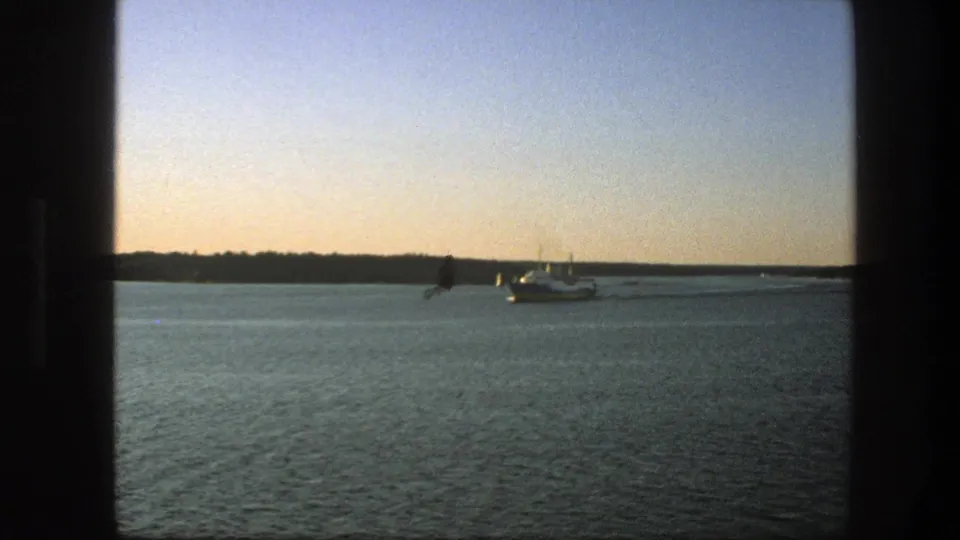 Wide 8mm view of the ferry farther away on Swedish waters, with a low dark shoreline and open sky.