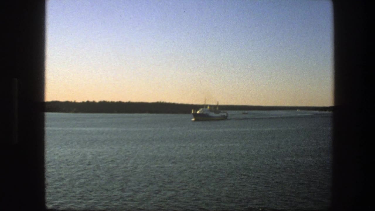 Ferry crossing a lake near a low wooded shoreline under a pale dusk sky.