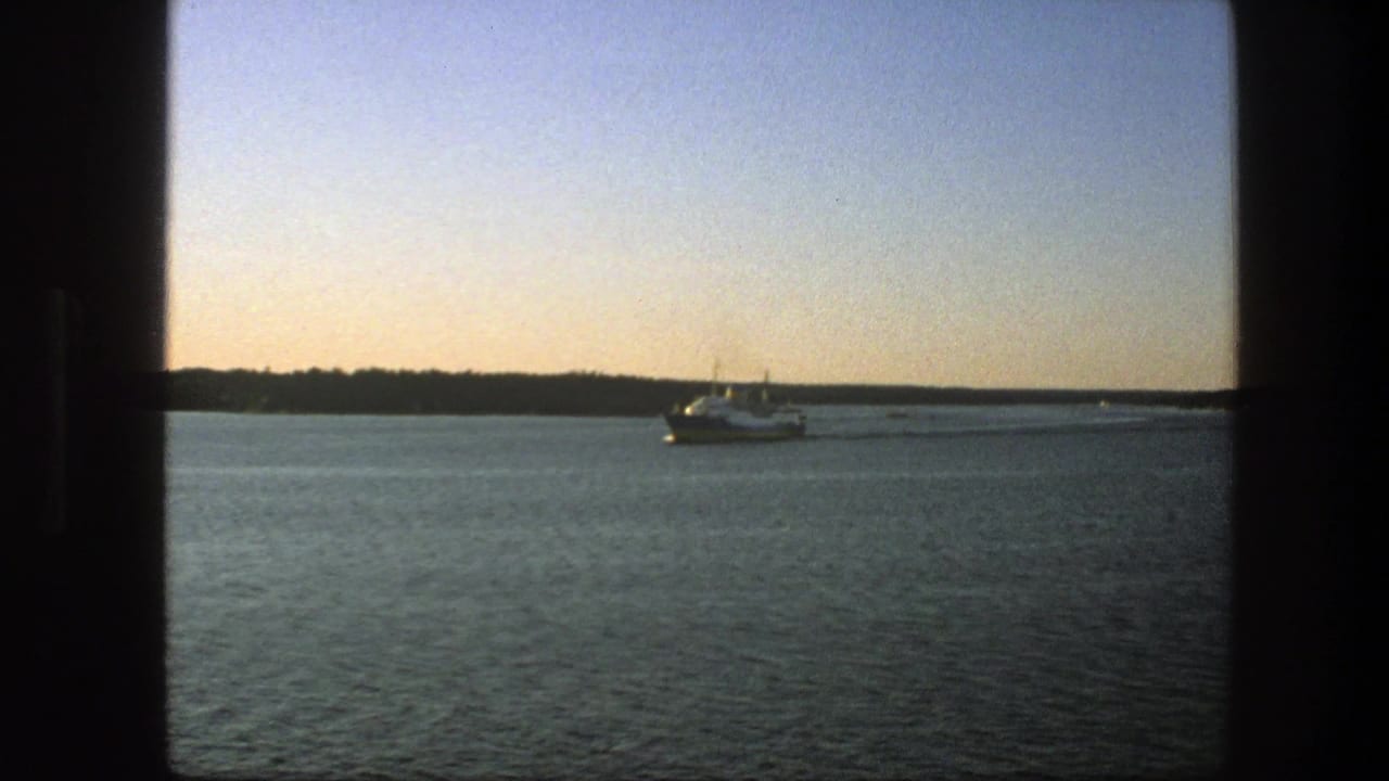 Small ferry on open lake water with a faint wake and wooded shore behind it.