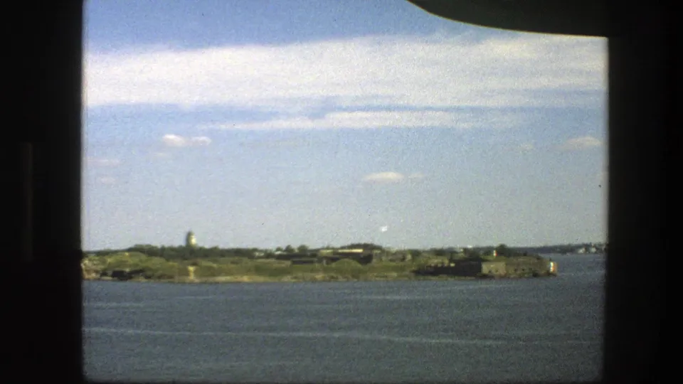 A 1975 8mm Sweden coastal view shows a grassy island, tower-like landmark, and low structures seen from a moving boat.