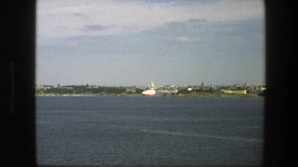 The closing 1975 Sweden frame holds on open water with a red-and-white ship and distant shoreline buildings beneath light cloud.