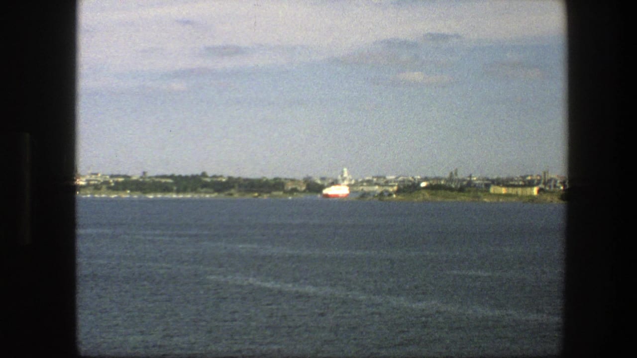 Calm blue water with a distant shoreline and a small red and white boat, framed by dark window edges.