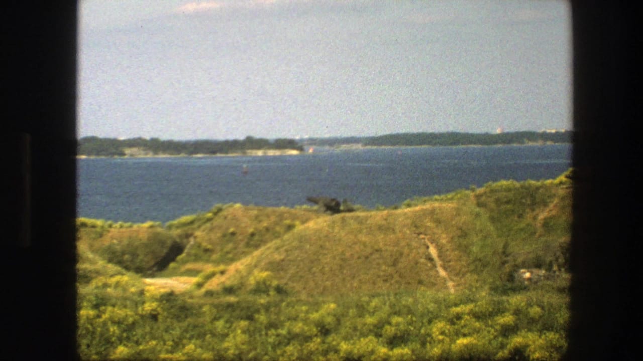 Coastal water and grassy hills seen through a dark window frame.