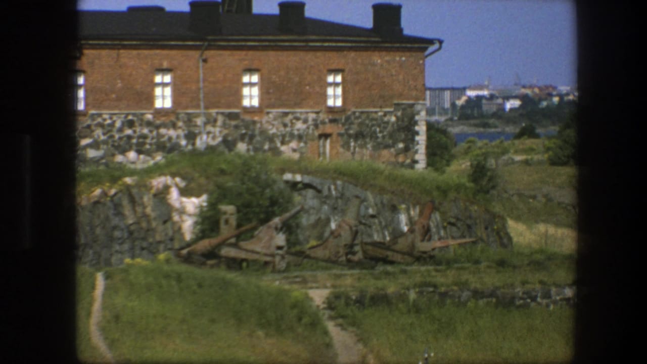 Brick-and-stone building above rocks and grass near coastal water.