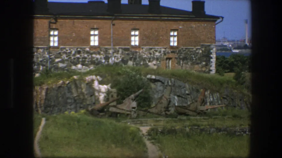 1975 Sweden frame of a coastal fort-like site with brick walls, stonework, grassy rocks, a path, and rusted artillery.