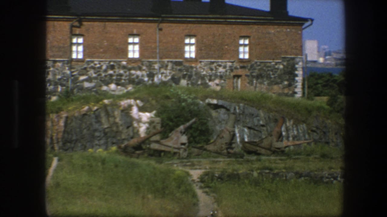 Brick building on a stone base above rocks and grass, with rusted artillery pieces in front.