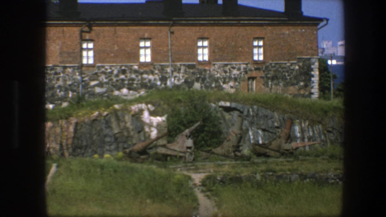 Brick building and stone wall above a grassy rocky slope with rusted artillery pieces.