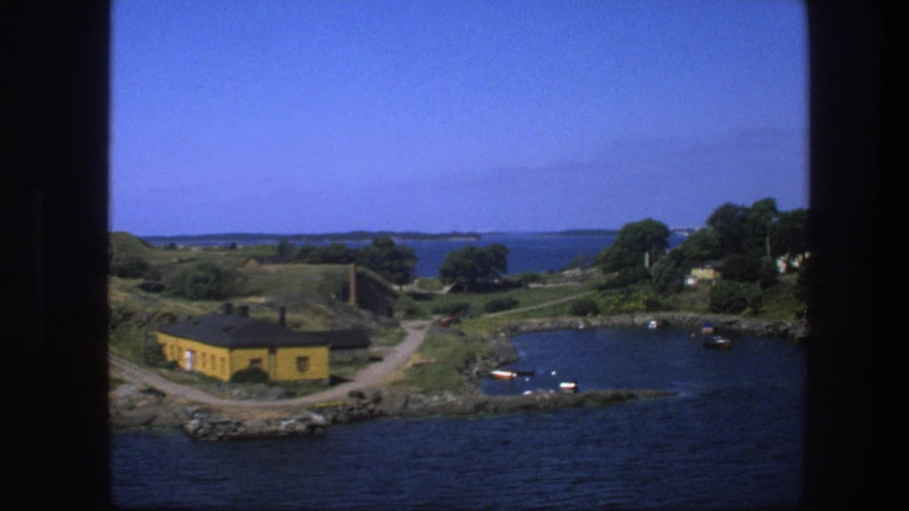 Bay landscape seen past dark vertical framing, with yellow building, boats, trees, and open water.