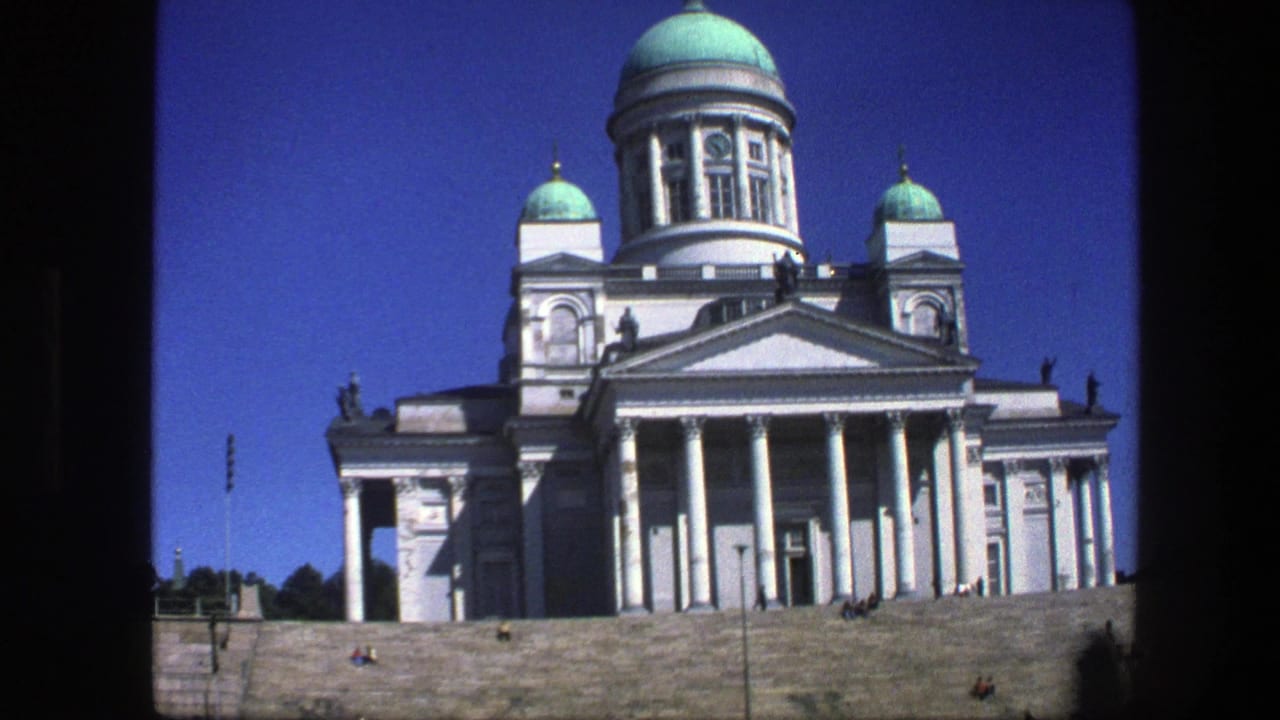 A 1970s 8mm frame shows a white neoclassical cathedral facade with green domes, columns, and broad stone steps below.