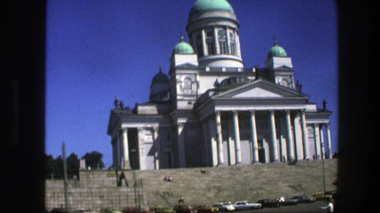 White cathedral with teal domes above stone steps and parked cars in a paved square.